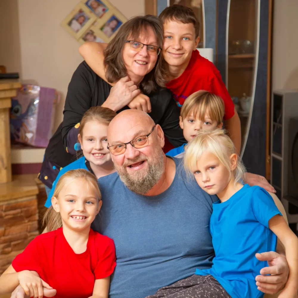 Rodzina pozująca do wspólnego zdjęcia w domu – uśmiechnięci dorośli i dzieci przytuleni do siebie.